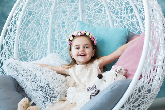 Happy girl sits in white hanging chair and spreads her hands on