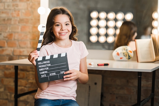 Happy girl sitting in makeup room holding clapper board