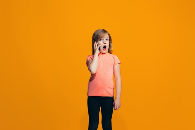 The happy girl standing and smiling against orange wall