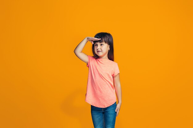 The happy girl standing and smiling against orange wall