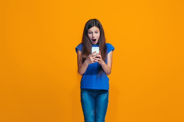 The happy girl standing and smiling against orange wall