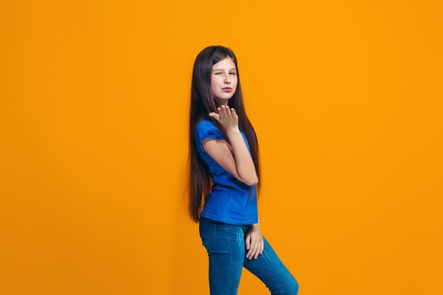 Счастливая девушка стоит и улыбается на оранжевой стене