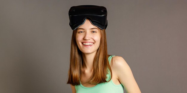 행복한 소녀는 VR 세트를 입고 회색 배경에서 웃고 있다