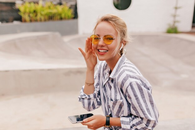 Happy girl with blond hair wearing orange glasses listening to music with earphones