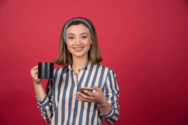 Happy girl with cup of tea holding cellphone