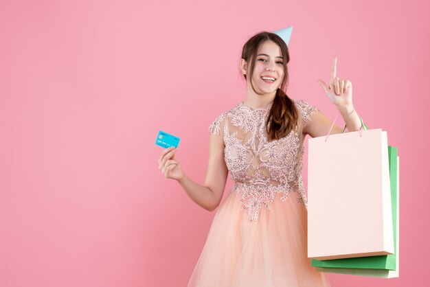 ピンクのパーティーキャップ保持カードとショッピングバッグを持つ幸せな女の子