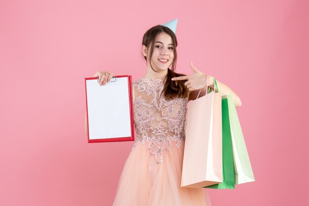 happy girl with party cap holding documents and shopping bags on pink