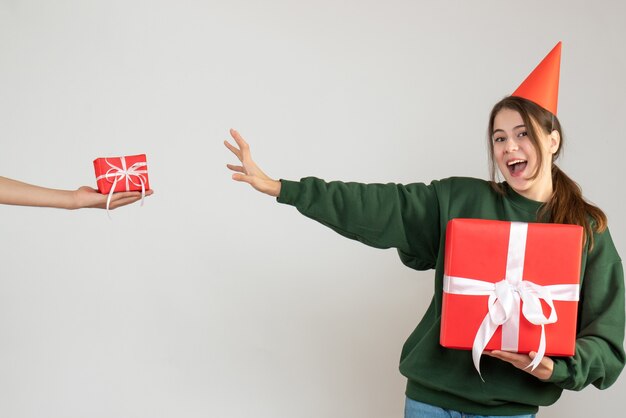 happy girl with party cap holding her christmas gift and human hand holding gift on white