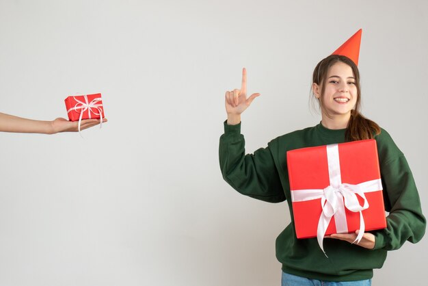 happy girl with party cap holding her christmas gift and human hand holding gift on white