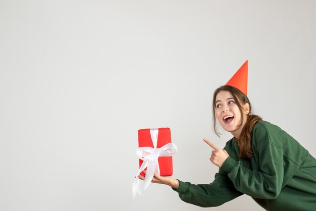 happy girl with party cap pointing at gift on white