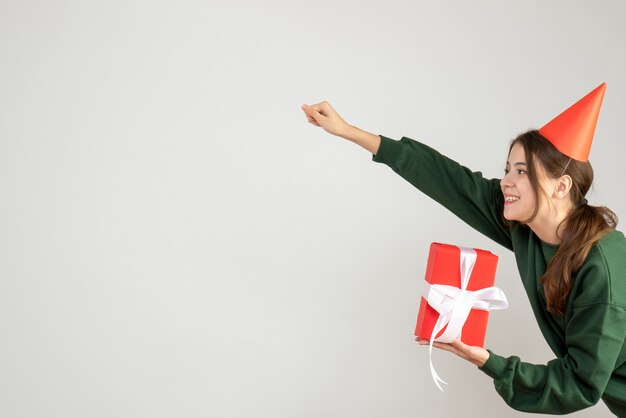 happy girl with party cap in super hero pose holding gift on white