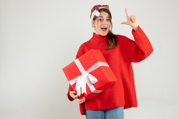 happy girl with santa hat holding gift finger pointing up on white