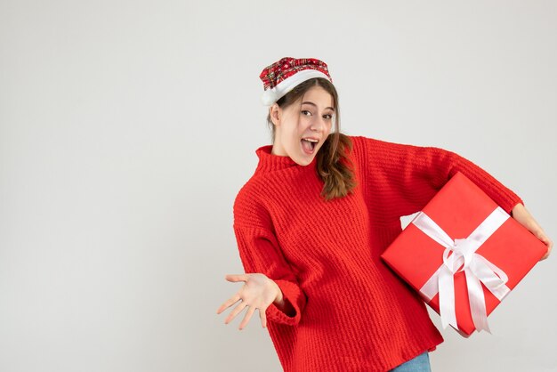 счастливая девушка в шляпе Санта держит подарок стоя на белом