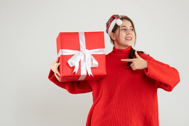 Ragazza felice con il cappello della santa che tiene il dito presente che punta la casella in piedi su bianco