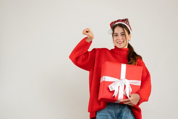 happy girl with santa hat holding present showing winning gesture standing on white