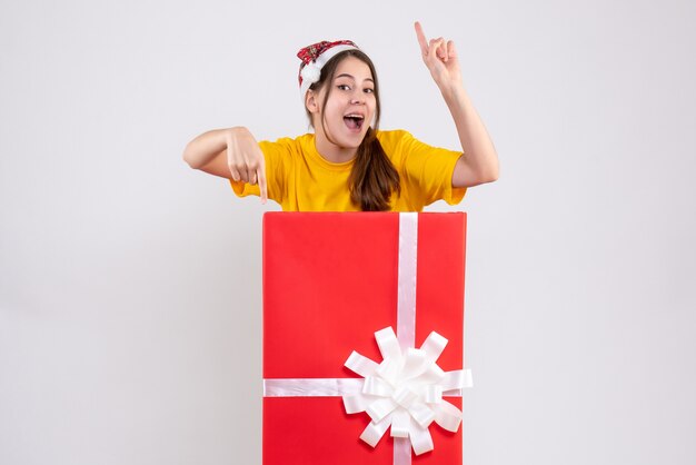 happy girl with santa hat standing behind big xmas present on white