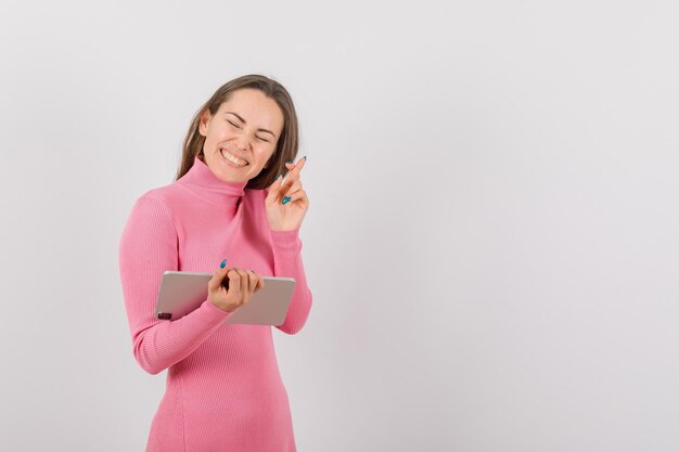 Happy girl with tablet computer is wishing by crossing finger on white background