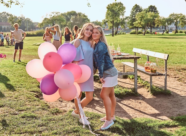 Foto gratuita fidanzate felici che posano con palloncini vicino a un tavolo per festeggiare un compleanno al parco all'aperto.