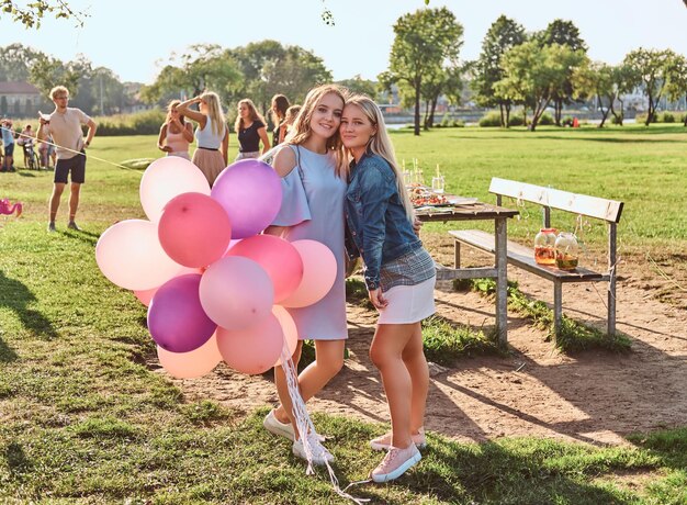 happy girlfriends posing with balloons near a table celebrating a birthday at the outdoor park.