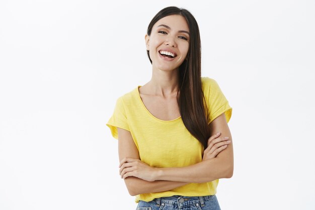 Happy good-looking slim woman with long dark hair holding hands crossed against chest in assertive, confident pose