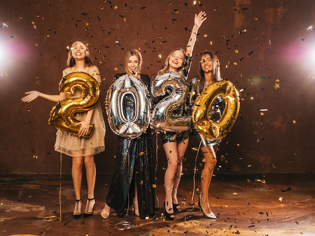 Happy Gorgeous Girls In Stylish Sexy Party Dresses Holding Gold and Silver 2020 Balloons