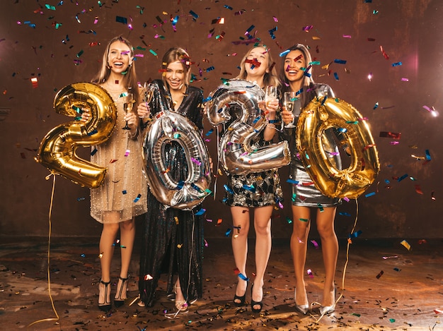 Ragazze bellissime felici in eleganti abiti da festa sexy con palloncini oro e argento 2020