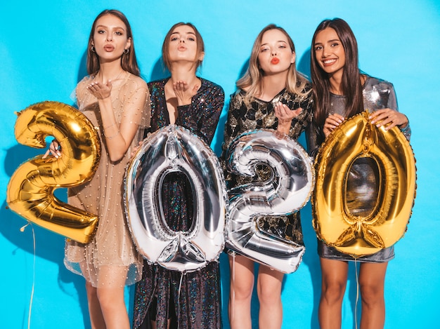 Happy Gorgeous Girls In Stylish Sexy Party Dresses Holding Gold and Silver 2020 Balloons