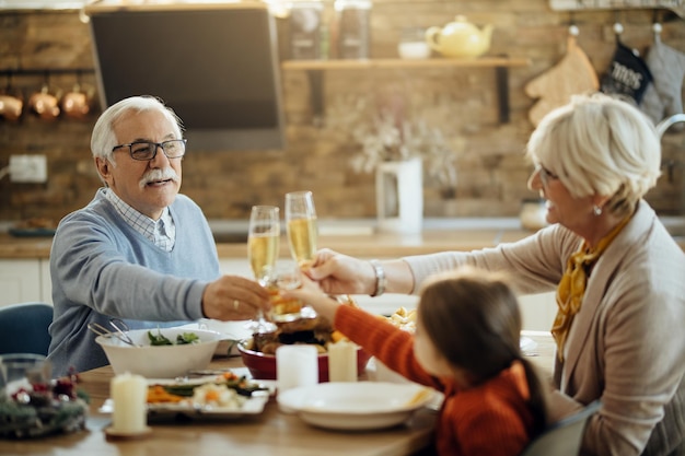 Счастливые бабушка и дедушка и внучка пьют тосты во время обеда в честь Дня Благодарения дома