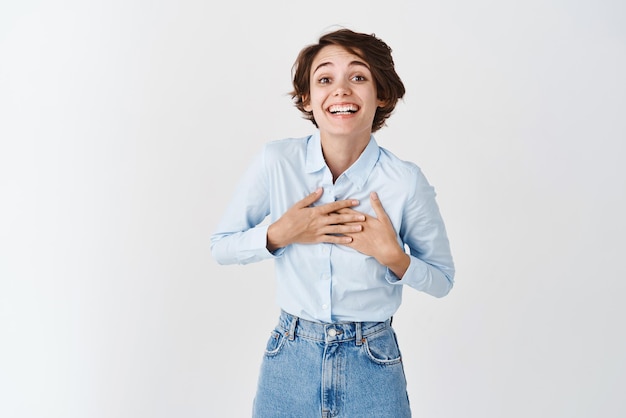 Happy grateful woman touching chest and smiling thanking you appreciate help standing pleased on white background