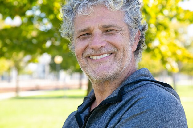 Happy grey haired man in sportswear standing outside, a and smiling. Closeup shot. Mature sporty person or active lifestyle concept