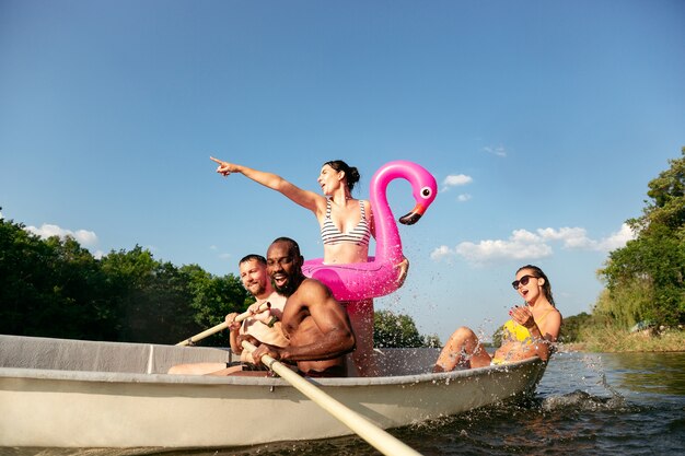 웃음과 강에서 수영하는 동안 재미 친구의 행복 그룹. 화창한 날에 강변에서 보트에 수영복에 즐거운 남녀. 여름, 우정, 리조트, 주말 개념.