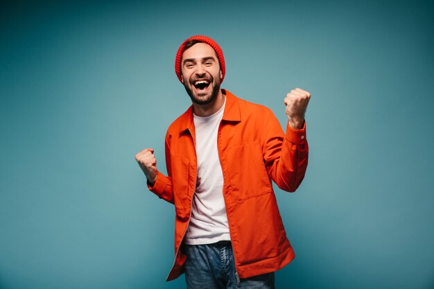 Happy guy in bright outfit laughing and posing on blue background