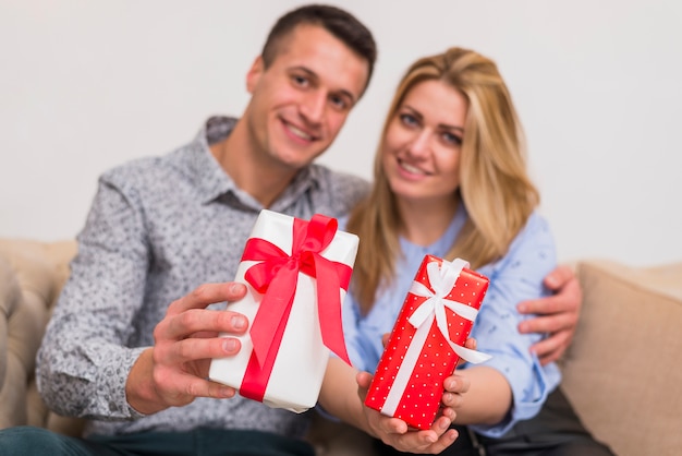 Free photo happy guy embracing smiling lady and showing presents on settee