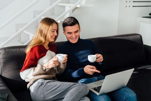 Happy guy and girl looking at laptop screen, watching a movie, having fun together