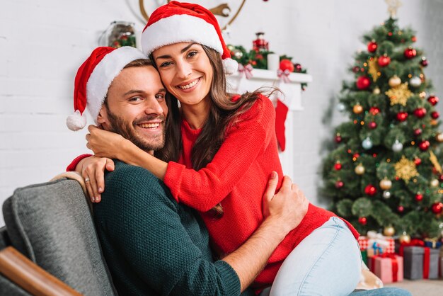 Happy guy and lady in party hats embracing on sofa