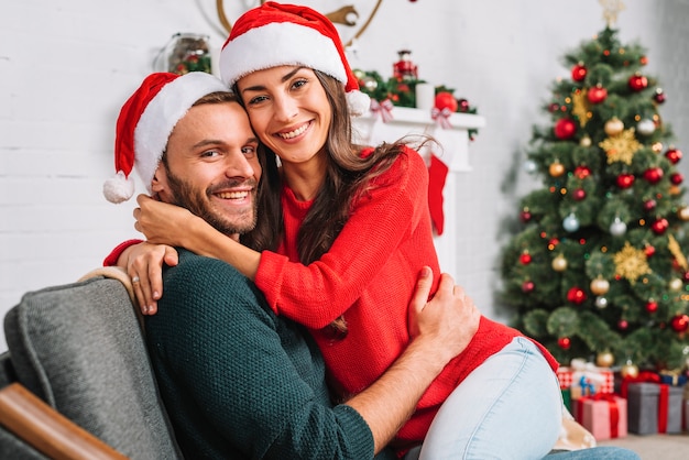 Happy guy and lady in party hats embracing on sofa