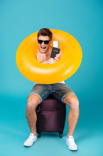 スーツケースの上に座ってサングラスで幸せな男