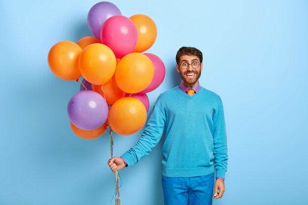 Happy guy with birthday hat and balloons posing in blue sweater