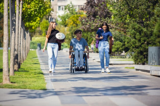 車椅子の幸せな障害者が屋外で楽器の生演奏をしている友達と時間を過ごしています。