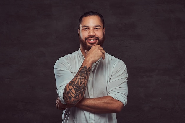 Счастливый красивый афроамериканский татуированный мужчина со стильными волосами и бородой в белой рубашке, держащий руку на подбородке.