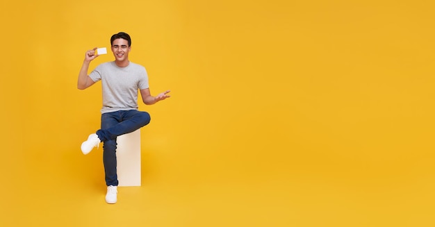 Free photo happy handsome asian man showing credit card for making payment or paying online business in hand isolated on yellow background