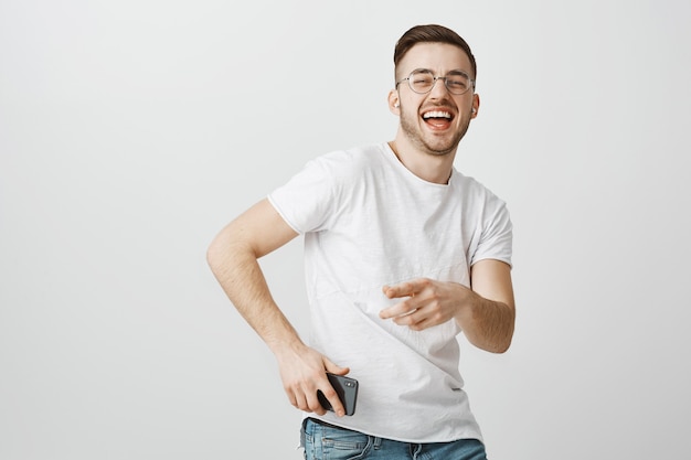 Бесплатное фото Счастливый красивый парень в очках танцует под музыку в беспроводных наушниках с мобильным телефоном в руке