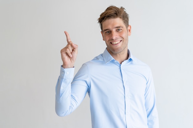 Happy handsome guy pointing upwards and looking at camera