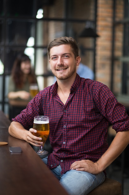 Foto gratuita felice uomo bello che tiene vetro di birra in barra