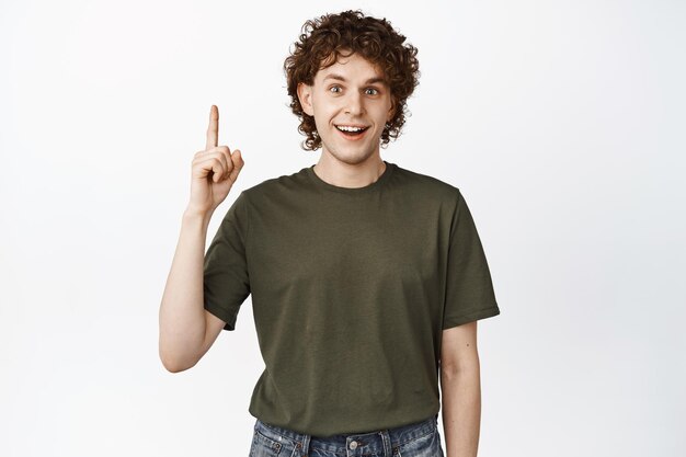 Happy handsome man pointing finger up smiling and looking excited showing advertisement standing over white background