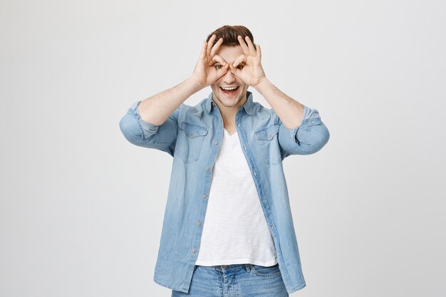 Happy handsome man showing okay sign over eyes, smiling