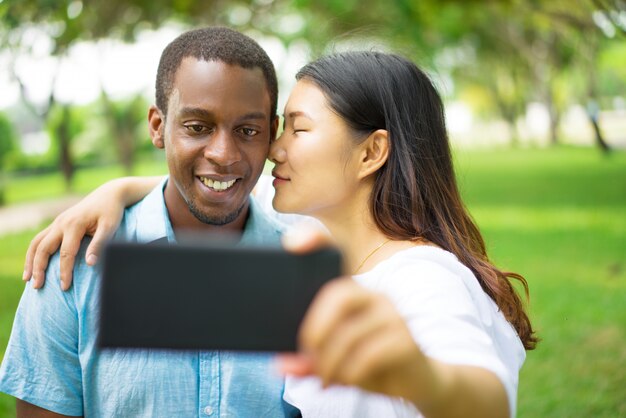 Happy handsome young African guy posing for selfie while his Asian girlfriend 