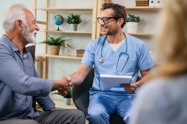 Happy healthcare worker shaking hands with senior man while being in a home visit