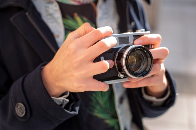 街の通りでレトロなカメラで写真を作る幸せな流行に敏感な女の子。旅行のコンセプト。コルスアップ