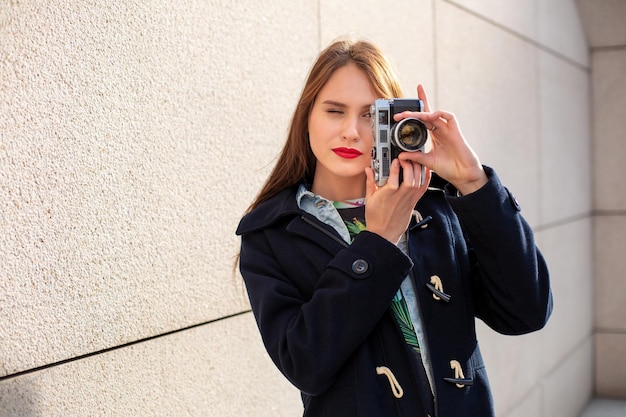 Счастливая девушка-хипстер делает фото с ретро-камерой на городской улице. Концепция путешествия